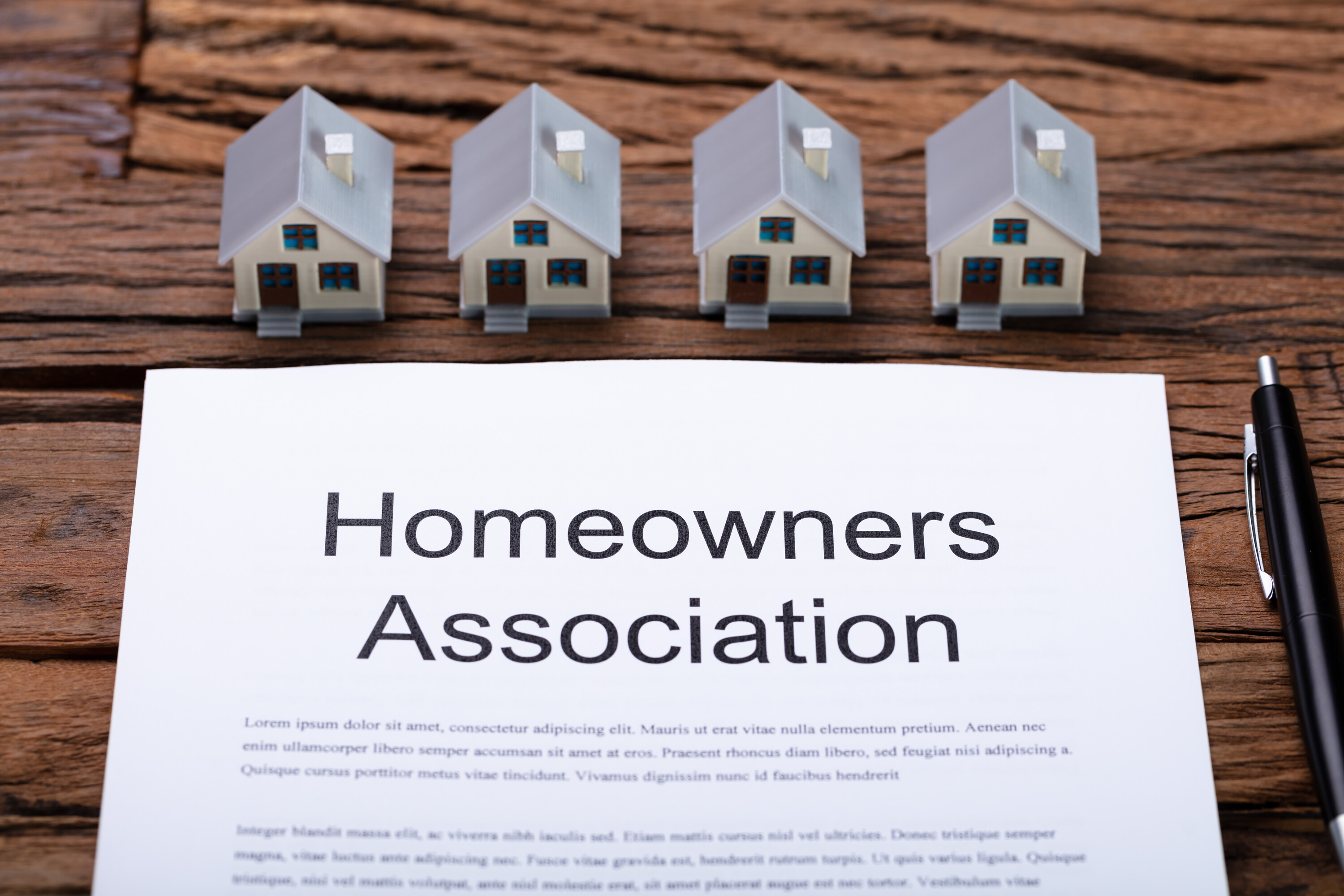 4 small cardboard houses lined up on table with a Homeowners association documents in front of them.