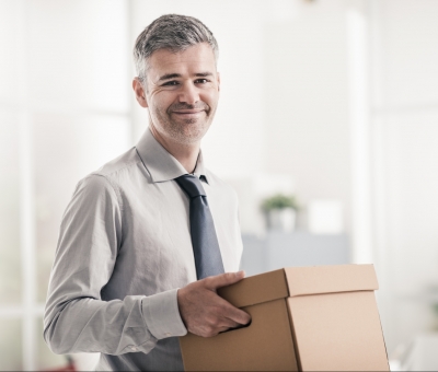 Man dressed in shirt and tie in an office holding a moving box
