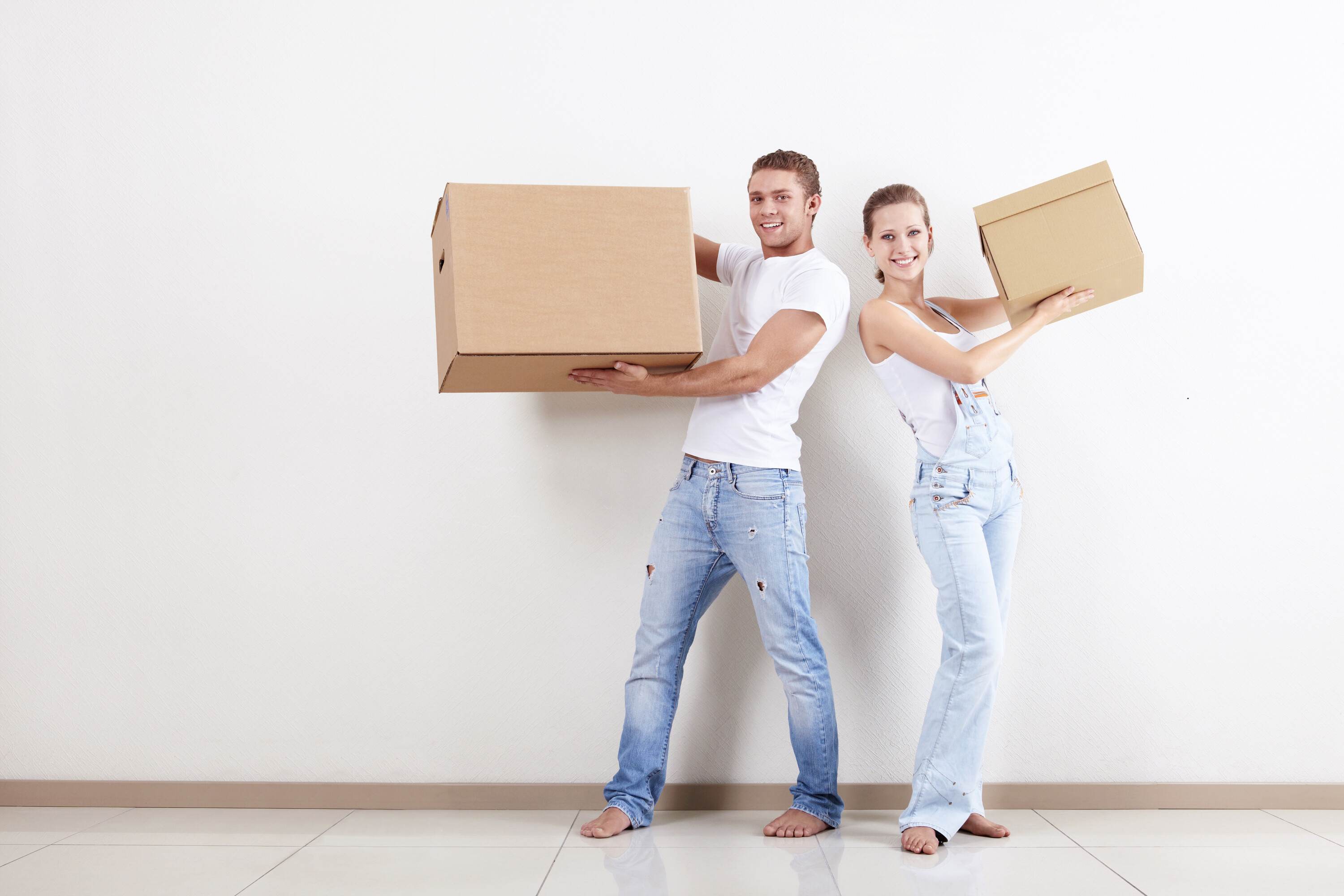 Man and woman standing back to back dresseed in jeans each holding moving boxes.