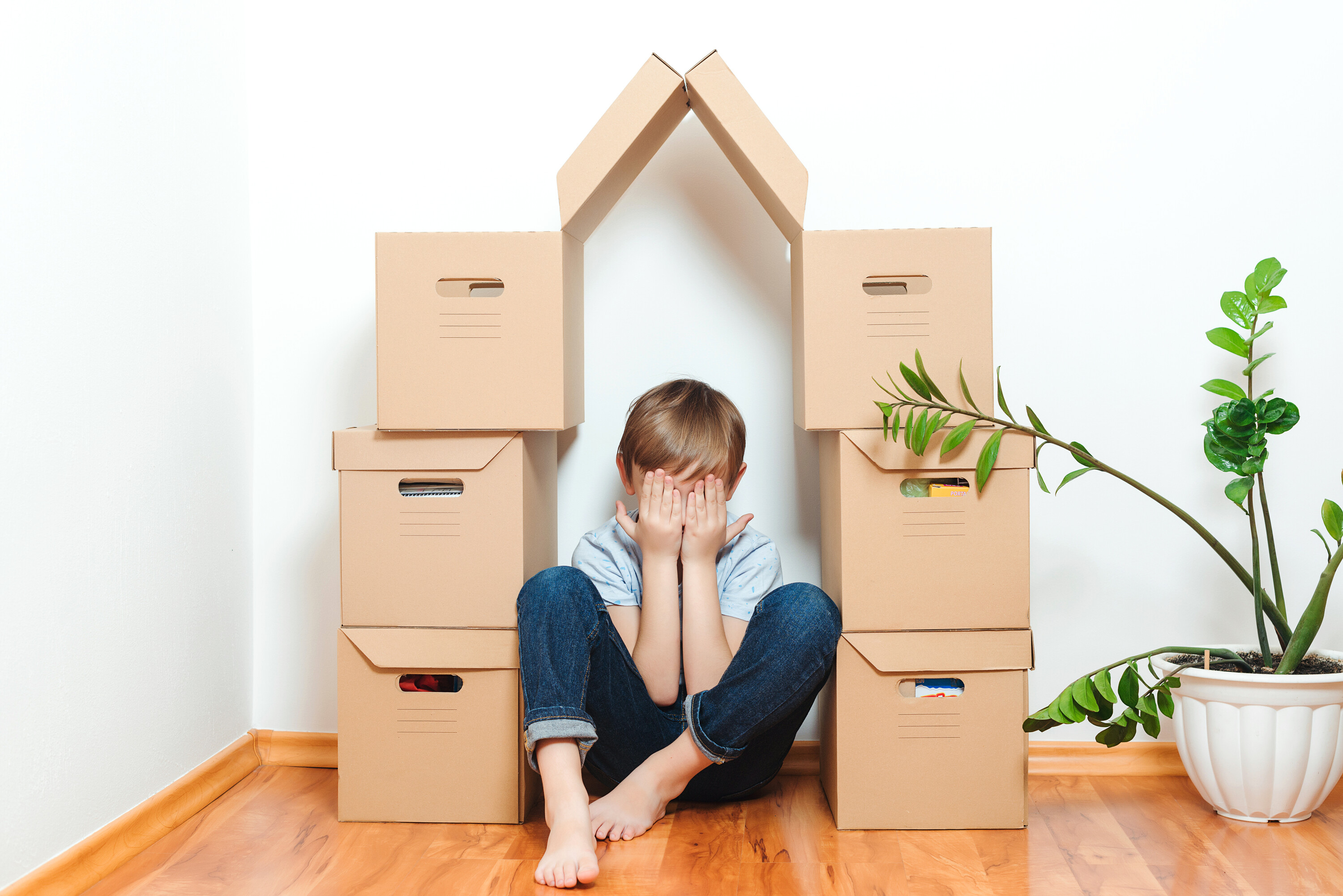 Young child with jeans and a tishirt sitting on the floor without shoes under a moving box pyramid.