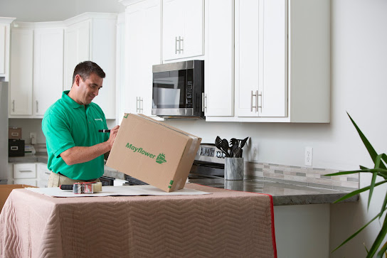 Mover in green shirt placing a Mayflower box on a kitchen counter.