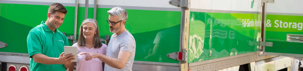 Mover showing a tablet to a smiling couple next to a Mayflower truck.